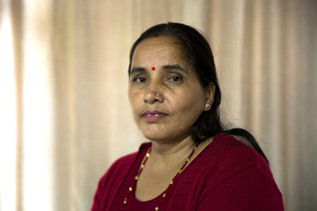Portrait of Sunita L. She has long black hair. She has a nose piercing, earring and a bindi on her forehead. She is wearing a long necklace with red and yellow stones. She is also wearing a red top with a red cardigan on top.