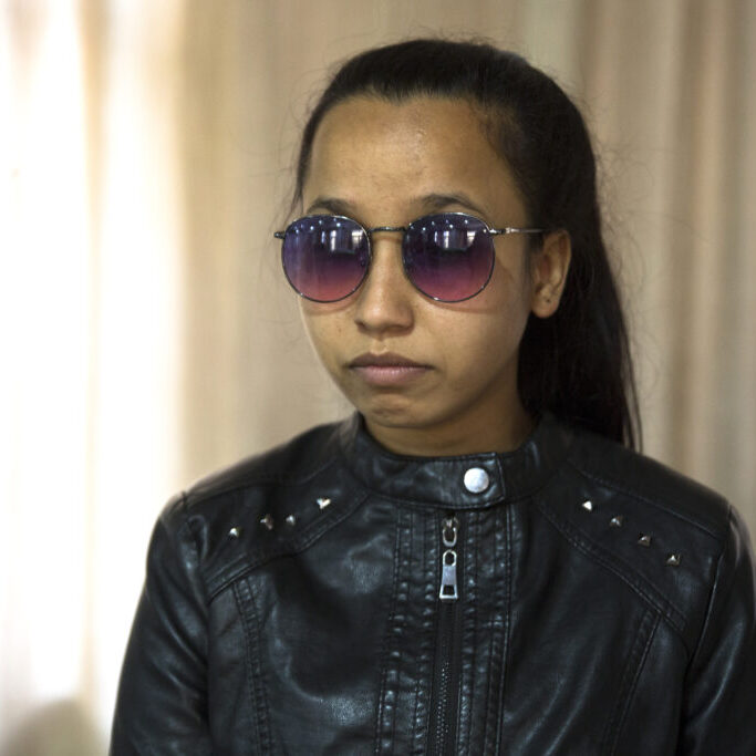 Portrait of Sunita N. She looks young and has long black hair tied back into a ponytail. She is wearing round sunglasses with purple-colored glasses and a silver frame. She is wearing a black leather jacket.